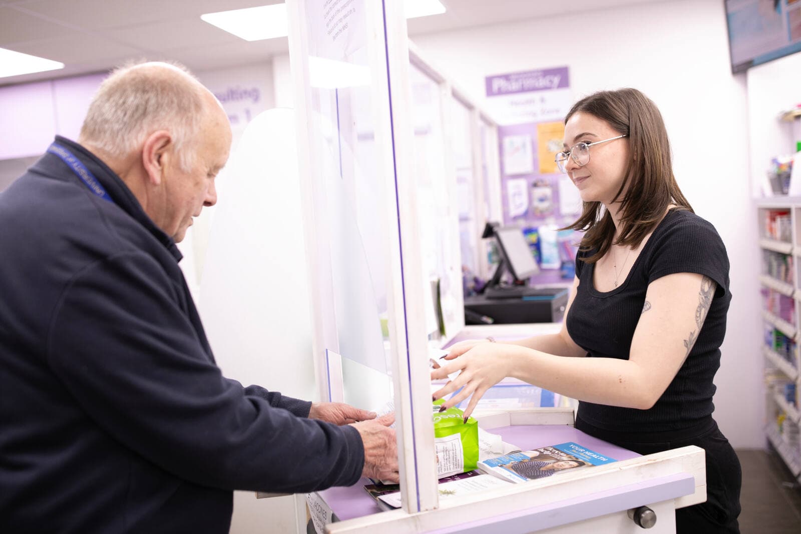 A pharmacist handing a prescription bag to a patient at the pharmacy counter